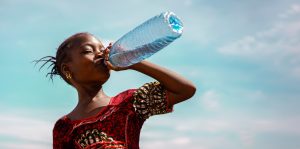 A young girl gracefully drinks water from a bottle, showcasing a moment of refreshment and vitality.