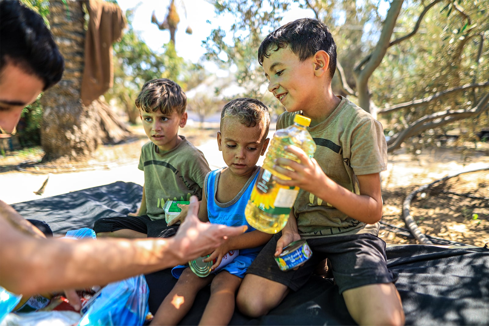 A man sits on the ground with two children, sharing a moment together while a bottle of water rests nearby.