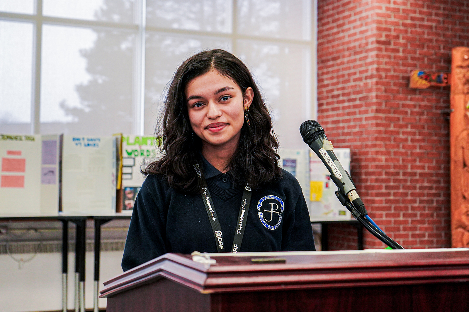 A girl stands confidently at a podium, addressing an audience with a microphone in front of her.
