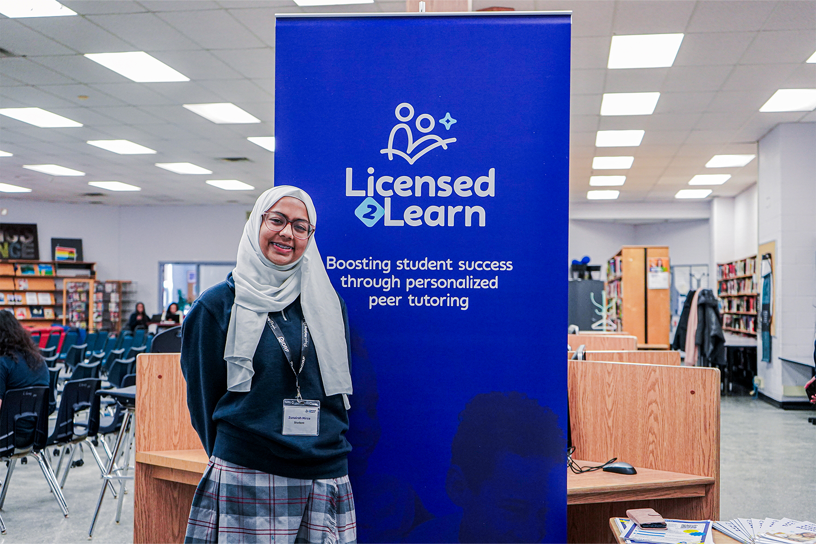 A woman in a hijab stands proudly in front of a sign that reads "Licensed Learn," symbolizing education and empowerment.