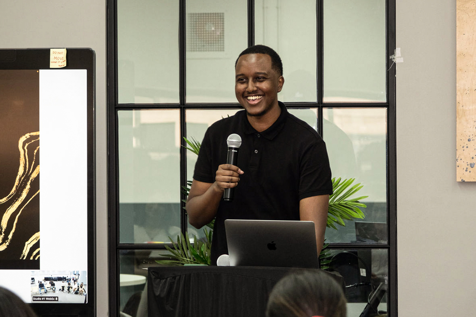A man in a black shirt stands confidently, holding a microphone, ready to speak or perform.