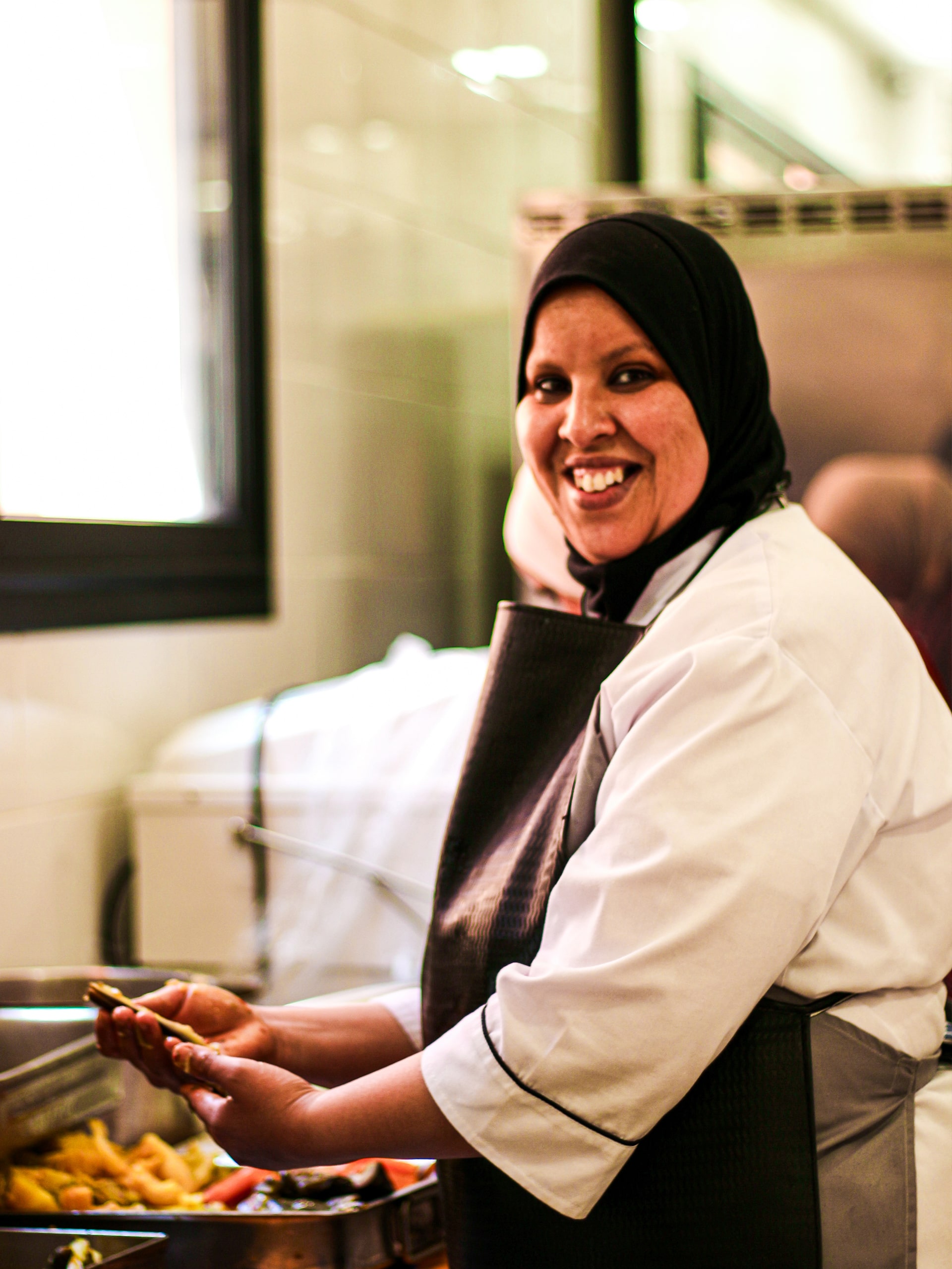 A woman stands in a modern kitchen, preparing a meal with fresh ingredients and a focused expression.