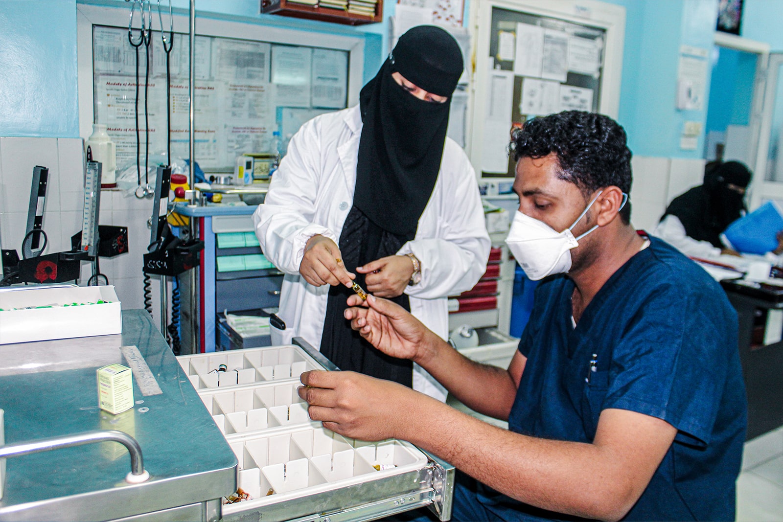 Woman and man in surgical masks carefully examine instruments on a tray, focused on their task in a clinical setting.
