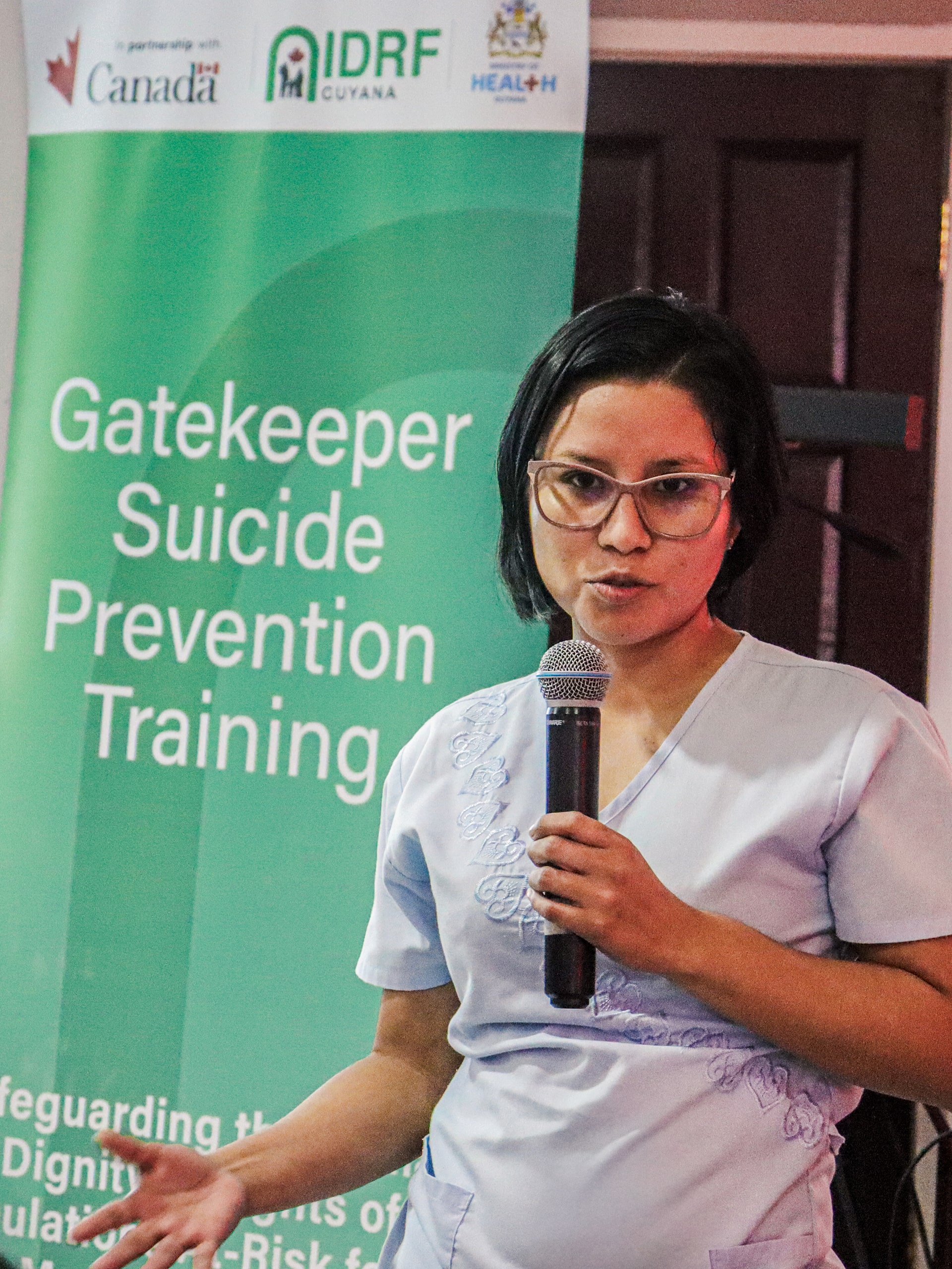 A woman in a white shirt confidently presents to an audience, sharing her insights and knowledge.