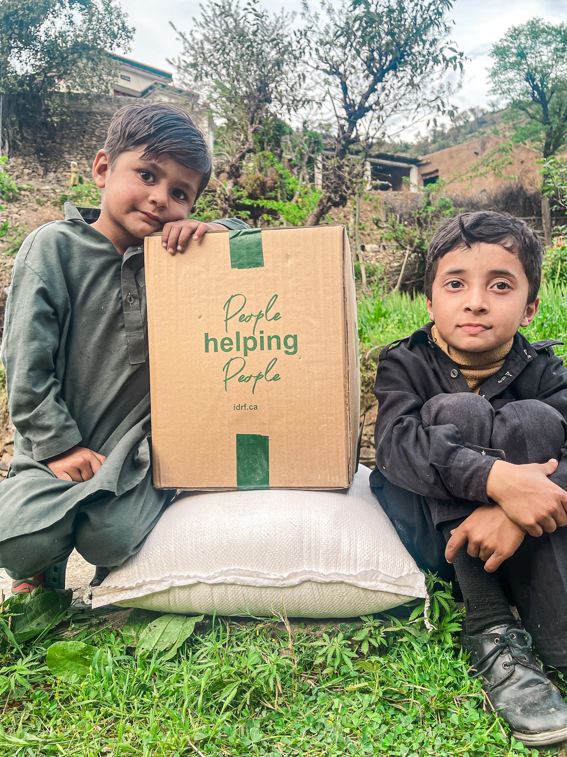 Two boys sit on a large pillow, engaged with a colorful box placed between them, sharing a moment of curiosity and joy.