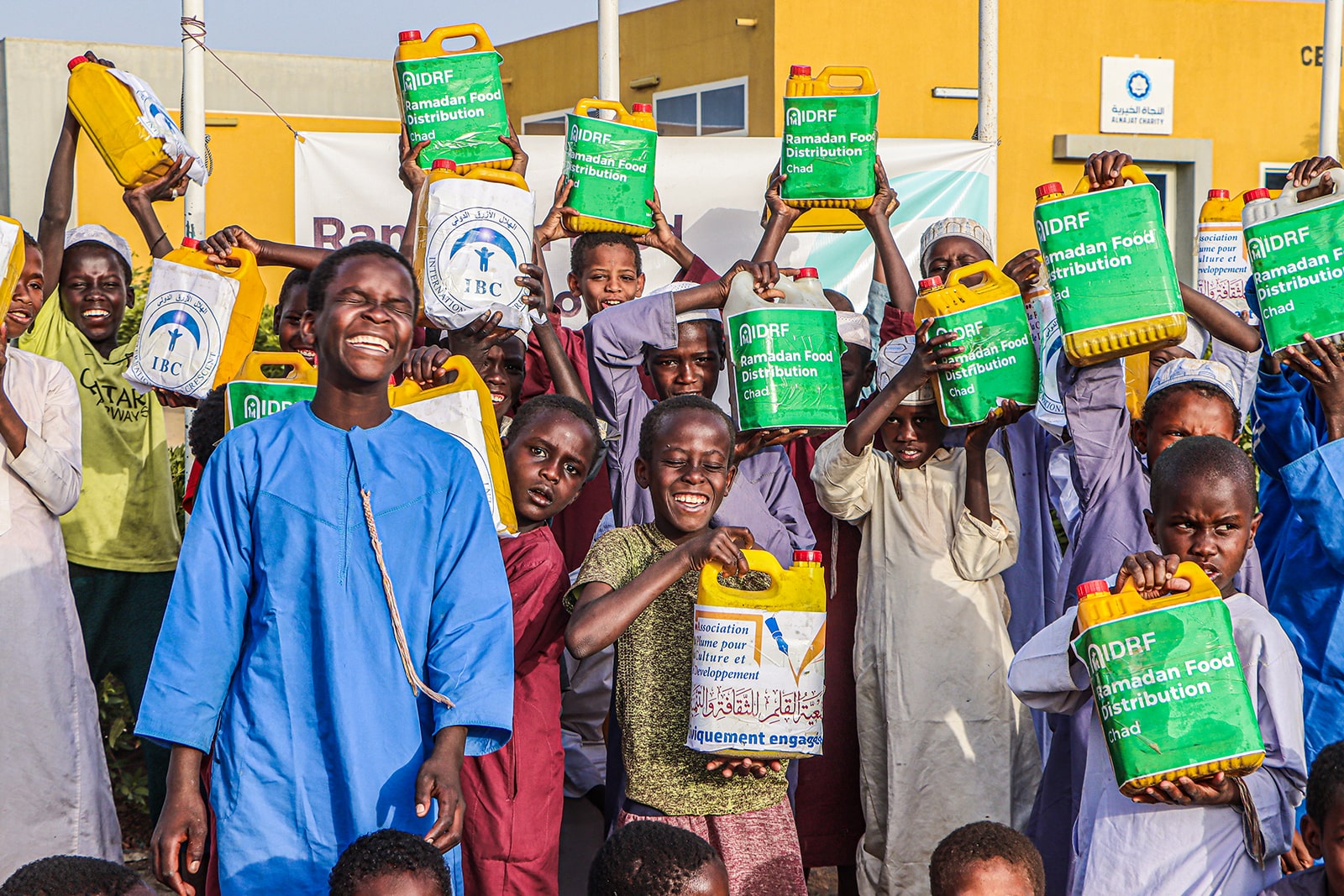 Children proudly display boxes of food in front of a community building, symbolizing hope and support for those in need.