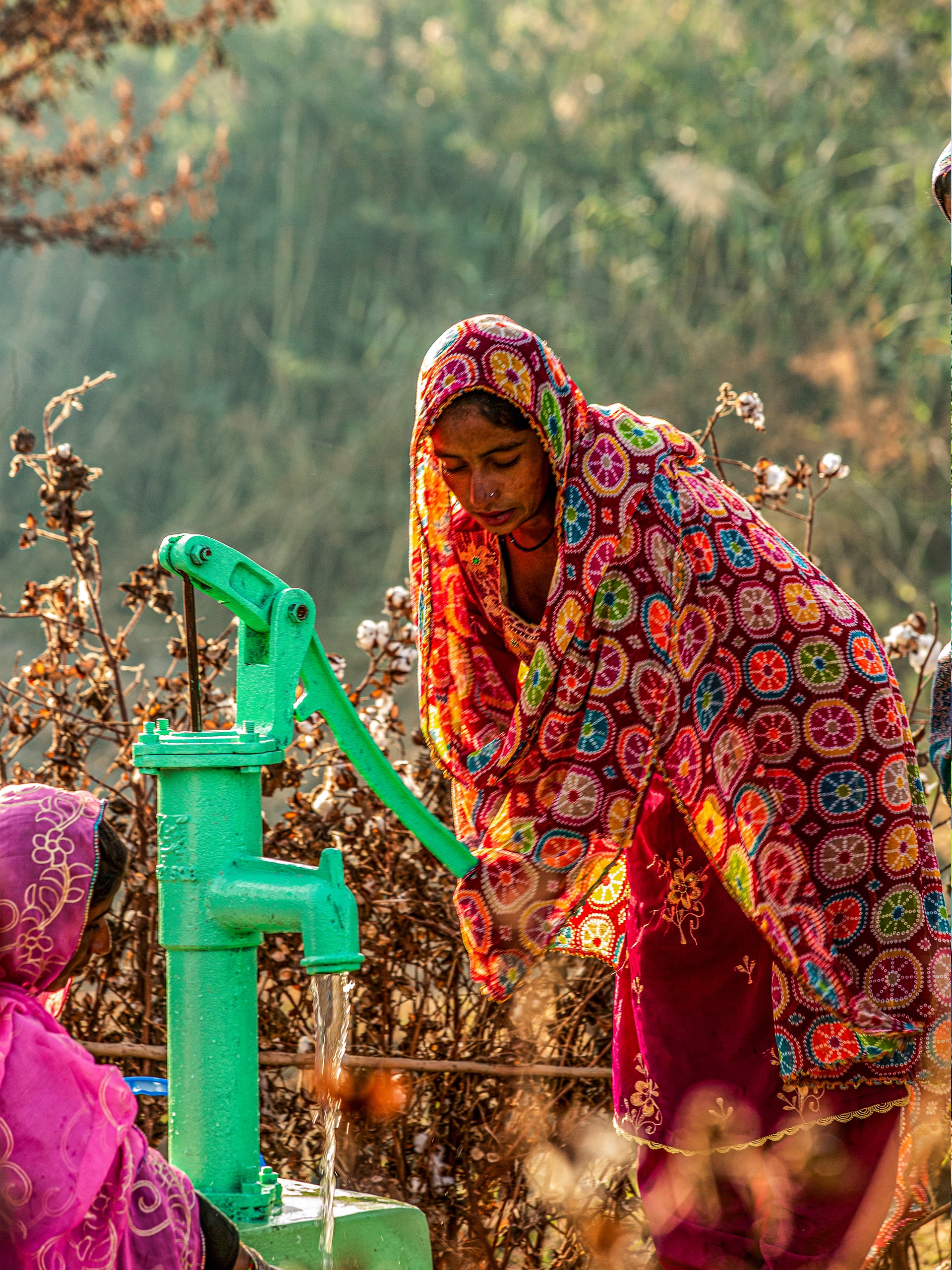 A woman in a vibrant dress operates a water pump, showcasing her strength and connection to the community's resources.