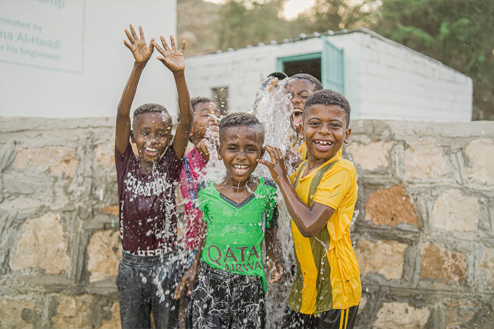A joyful group of children splashes and plays in a water fountain on a sunny day, enjoying the refreshing water.