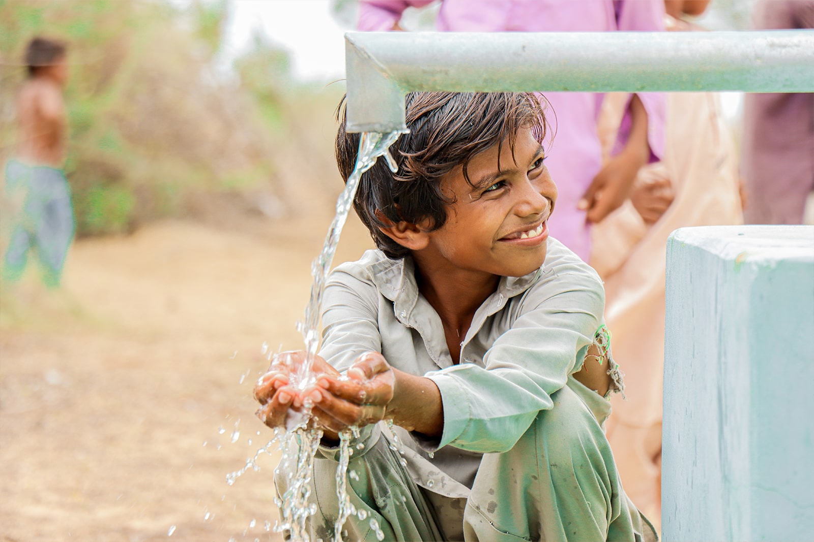 A young boy drinks water from a hand pump, showcasing the importance of access to clean water.