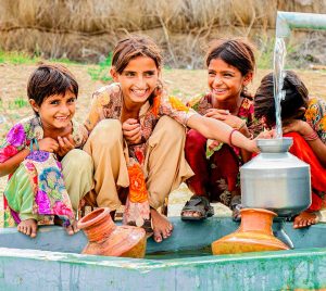 A group of girls gathers around a traditional water well, sharing stories and laughter in a serene outdoor setting.