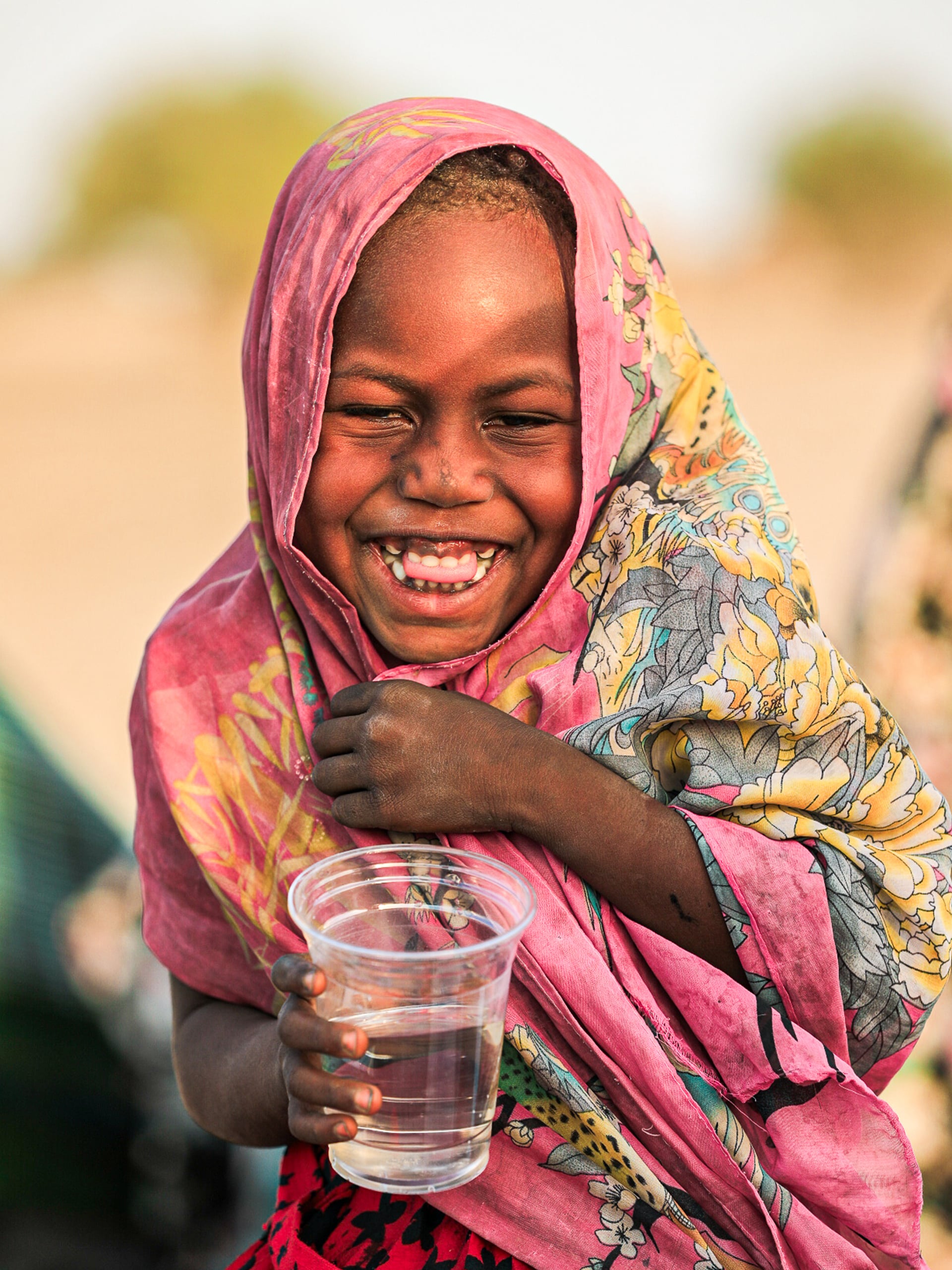 A smiling girl holds a glass of water, radiating joy and health in a bright, inviting setting.