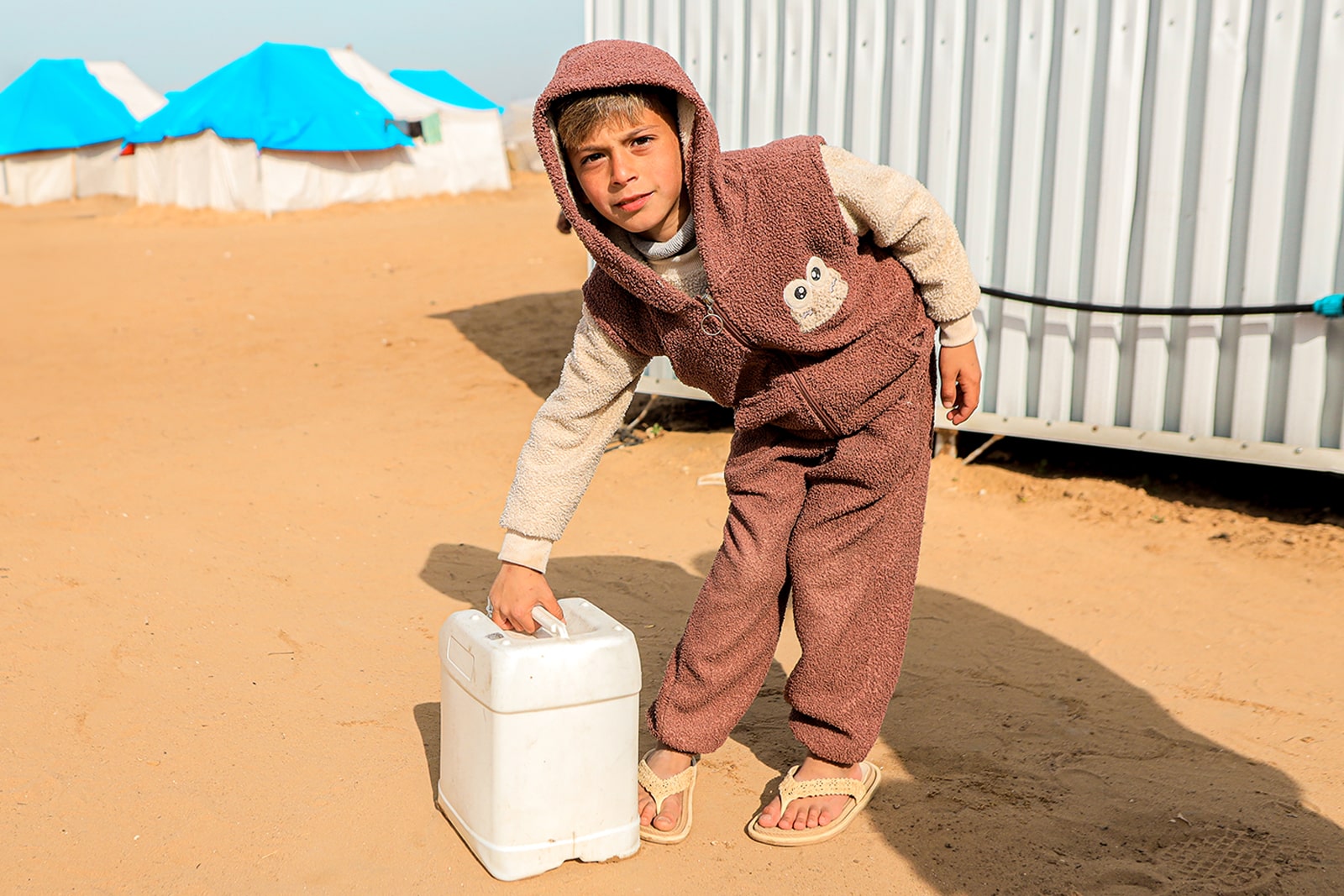 A young boy in a brown hoodie stands proudly, holding a cooler with a confident expression.