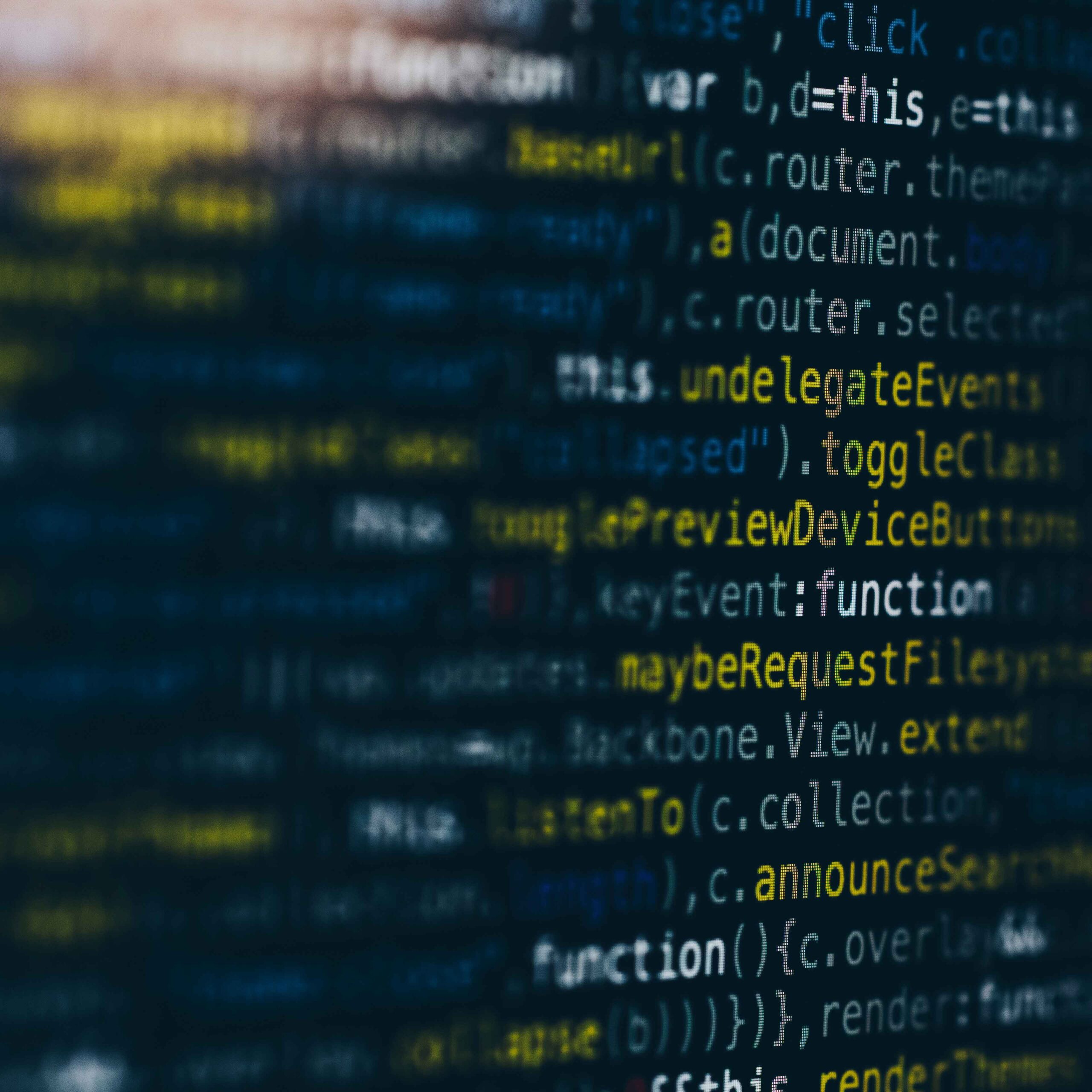 Close-up of a computer screen displaying lines of colorful, blurred code in shades of yellow, blue, and white on a dark background.
