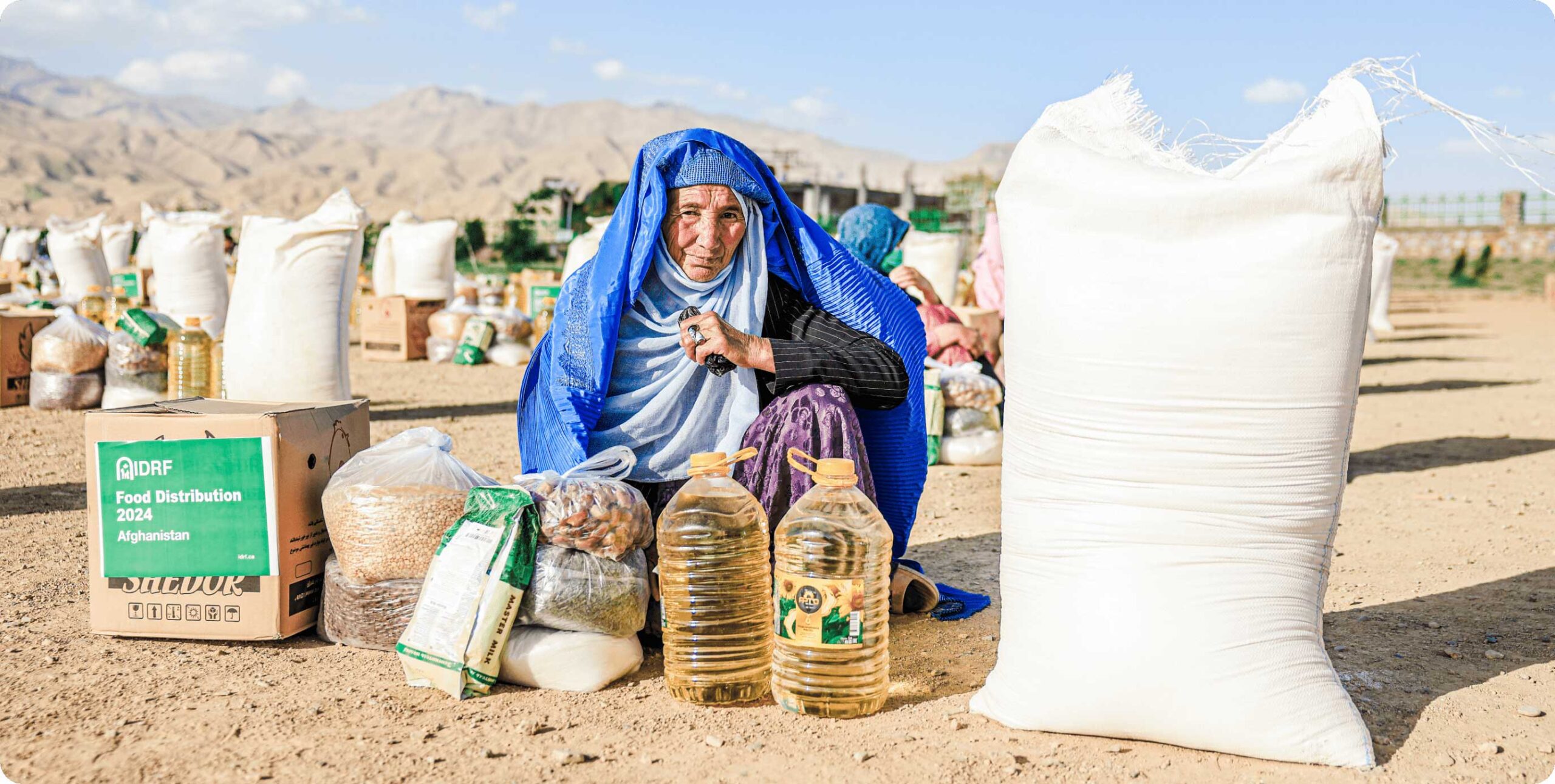 A woman seated on the ground surrounded by bags of food, reflecting resilience and strength in her situation.