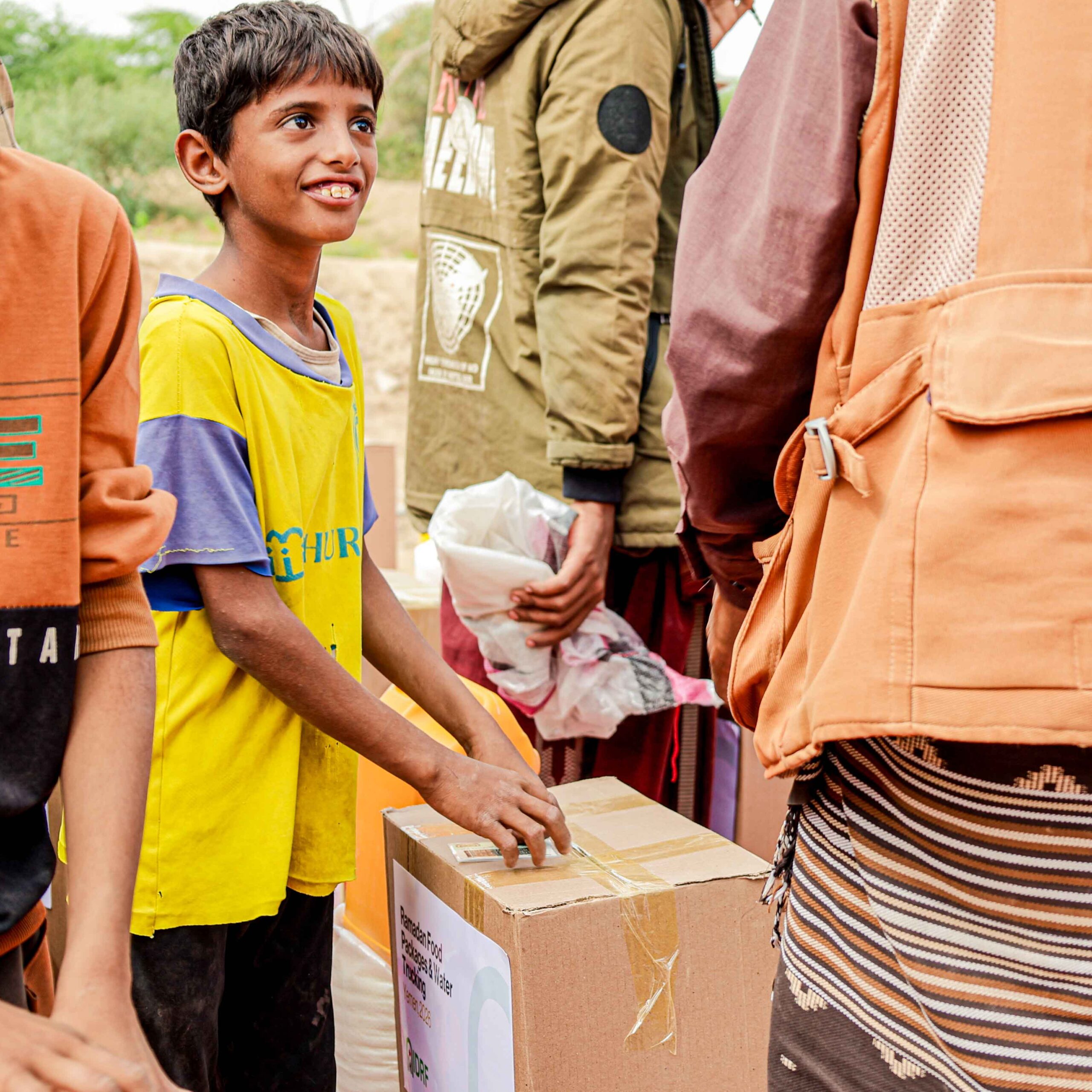 A group of children excitedly gathered around an open box, sharing smiles and looking at what's inside.