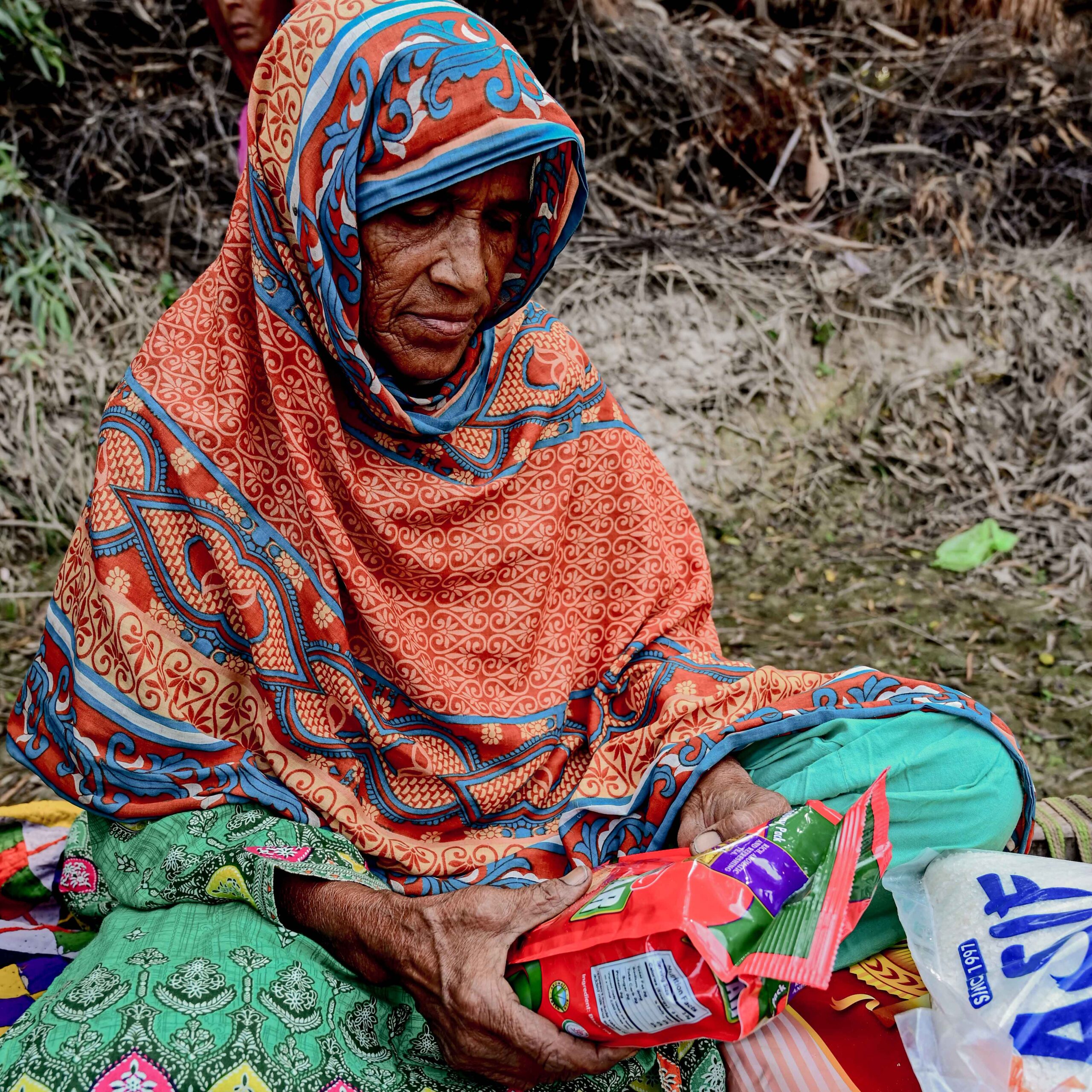 A woman sits on the ground, smiling while holding a bottle of water, enjoying a moment of relaxation.
