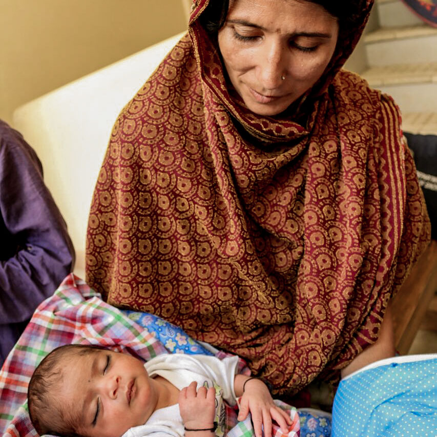 A woman lovingly cradles a baby in her arms, smiling gently at the child.